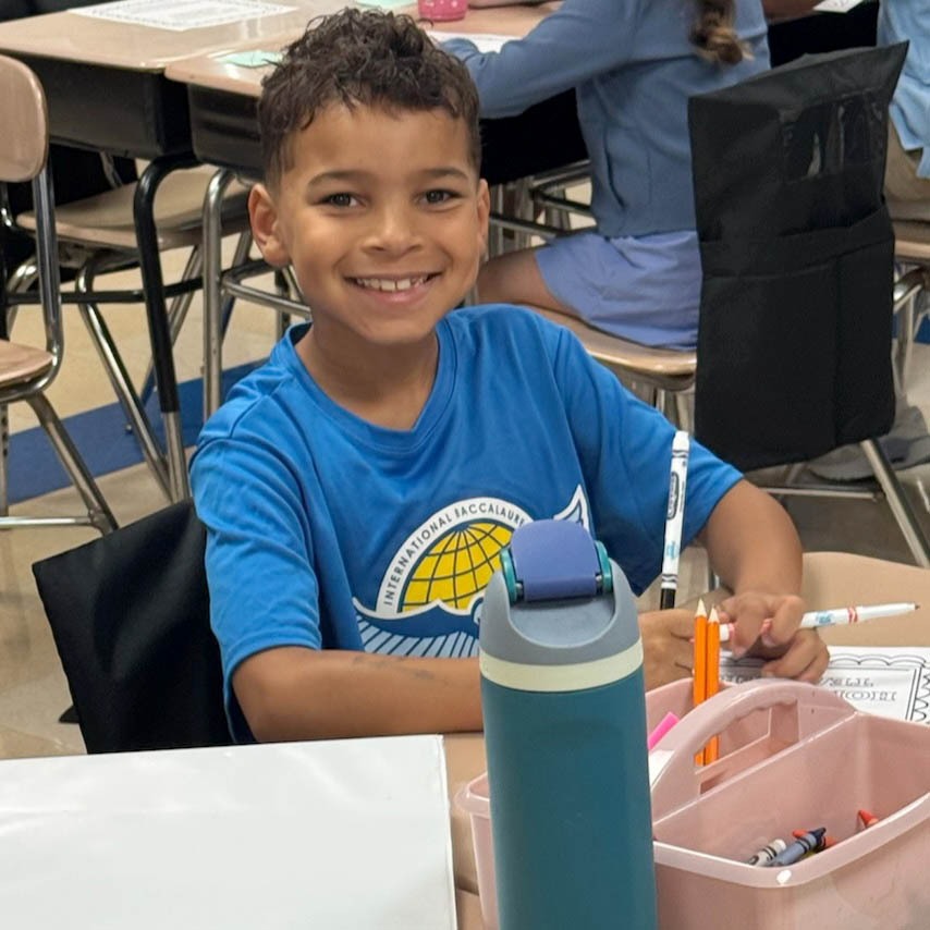 Boy sitting at desk, smiling at camera.
