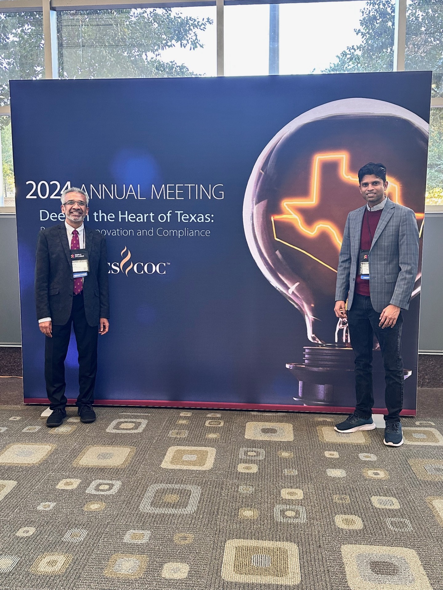 Two men standing in front of a promotional sign for a 2021 annual meeting.