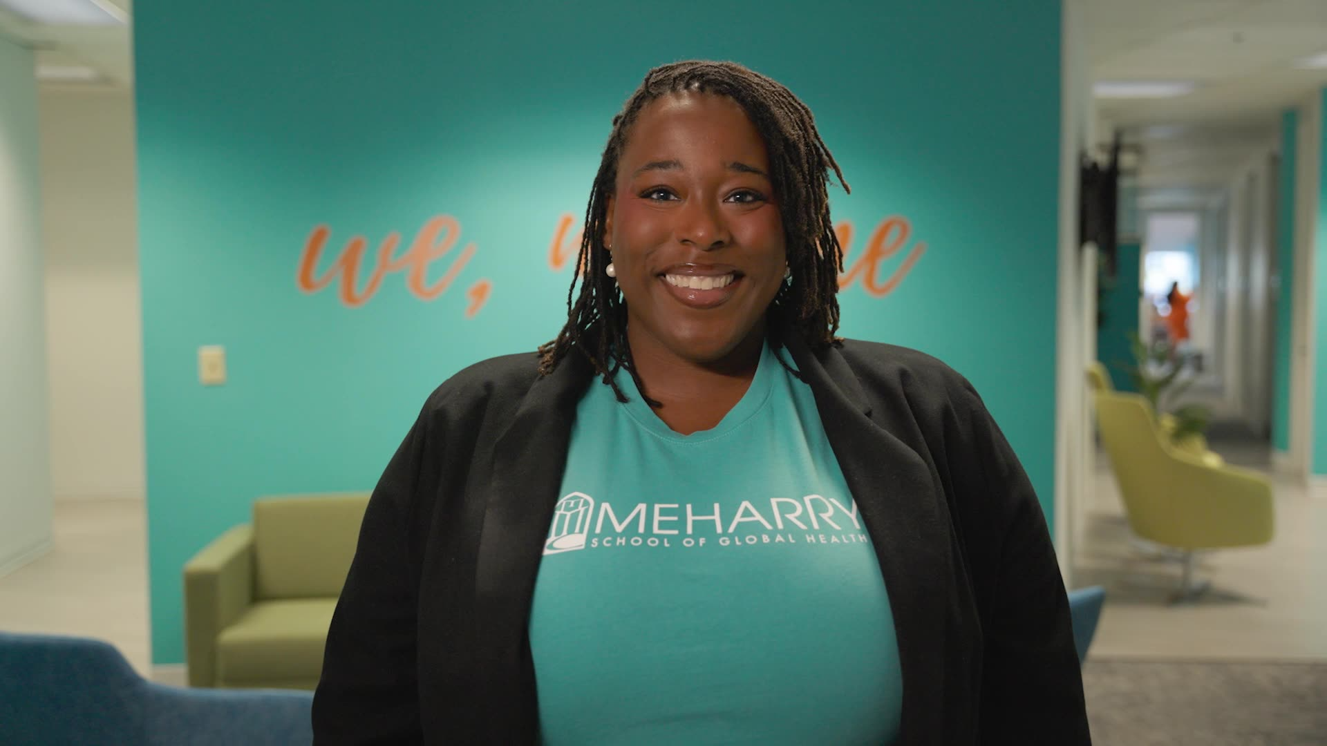 Woman standing in front of a blue wall with a sign. She is smiling and wearing a black shirt.