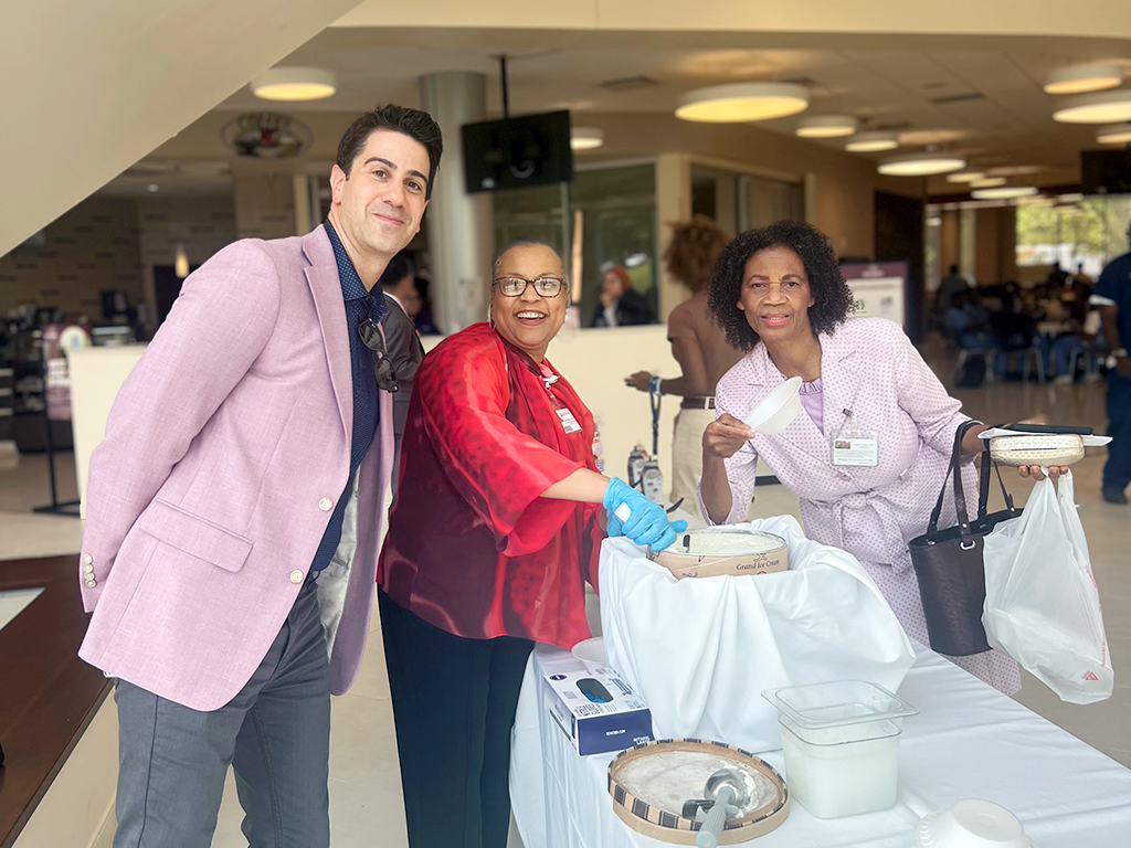 A man and woman posing at a table with food, another man standing behind them.