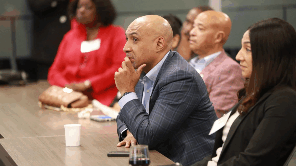 Man in suit sitting at conference table, looking thoughtful.