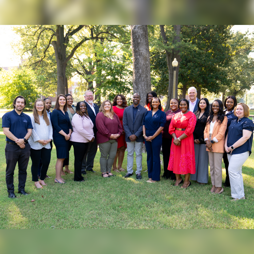 Group of people posing for a photo, smiling and standing in front of a tree.