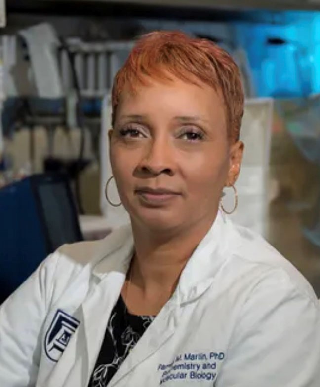 Woman in white lab coat, smiling, posing for photo.