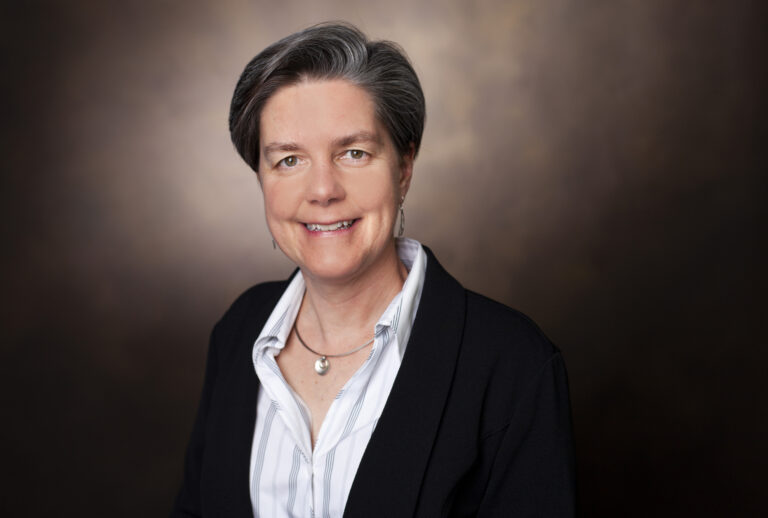 Woman in suit standing against backdrop.