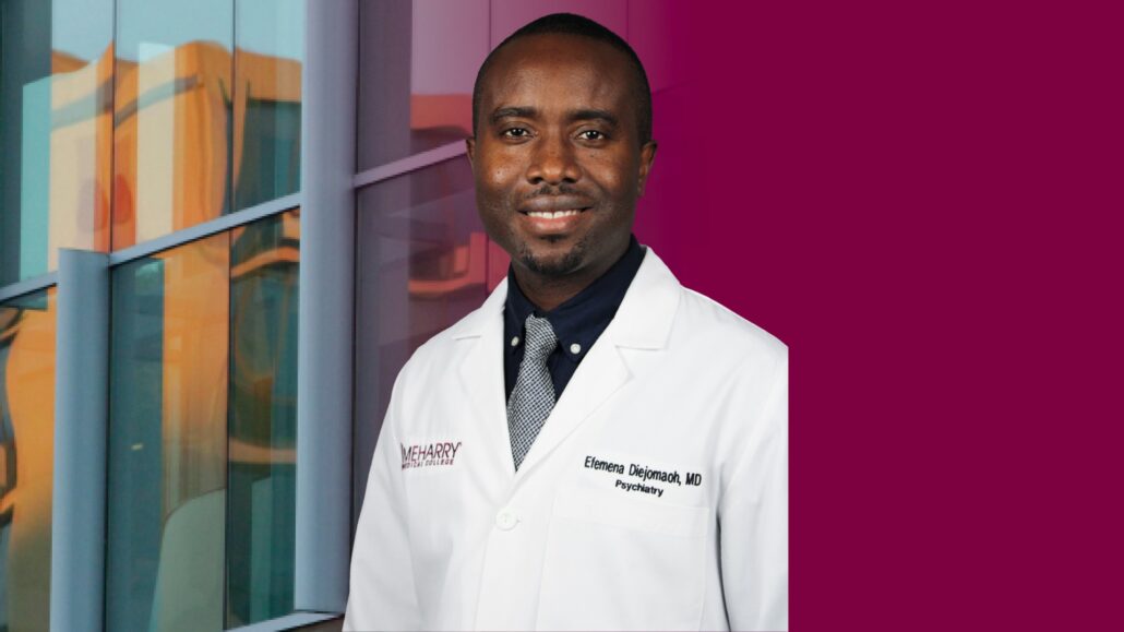 A man in a white coat standing in front of a window.
