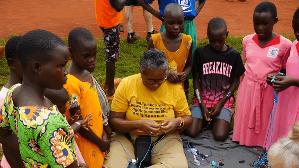 Group of people, mostly children, in colorful attire, gathered around a woman with a microphone, possibly at an event.