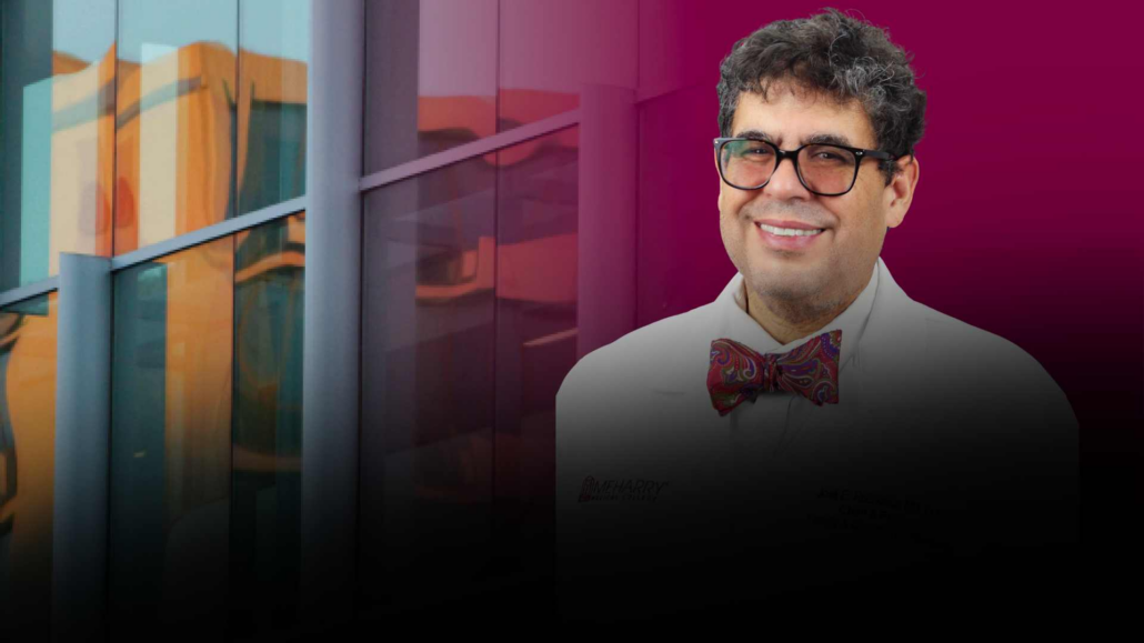 Man in glasses smiling, standing in front of a building.