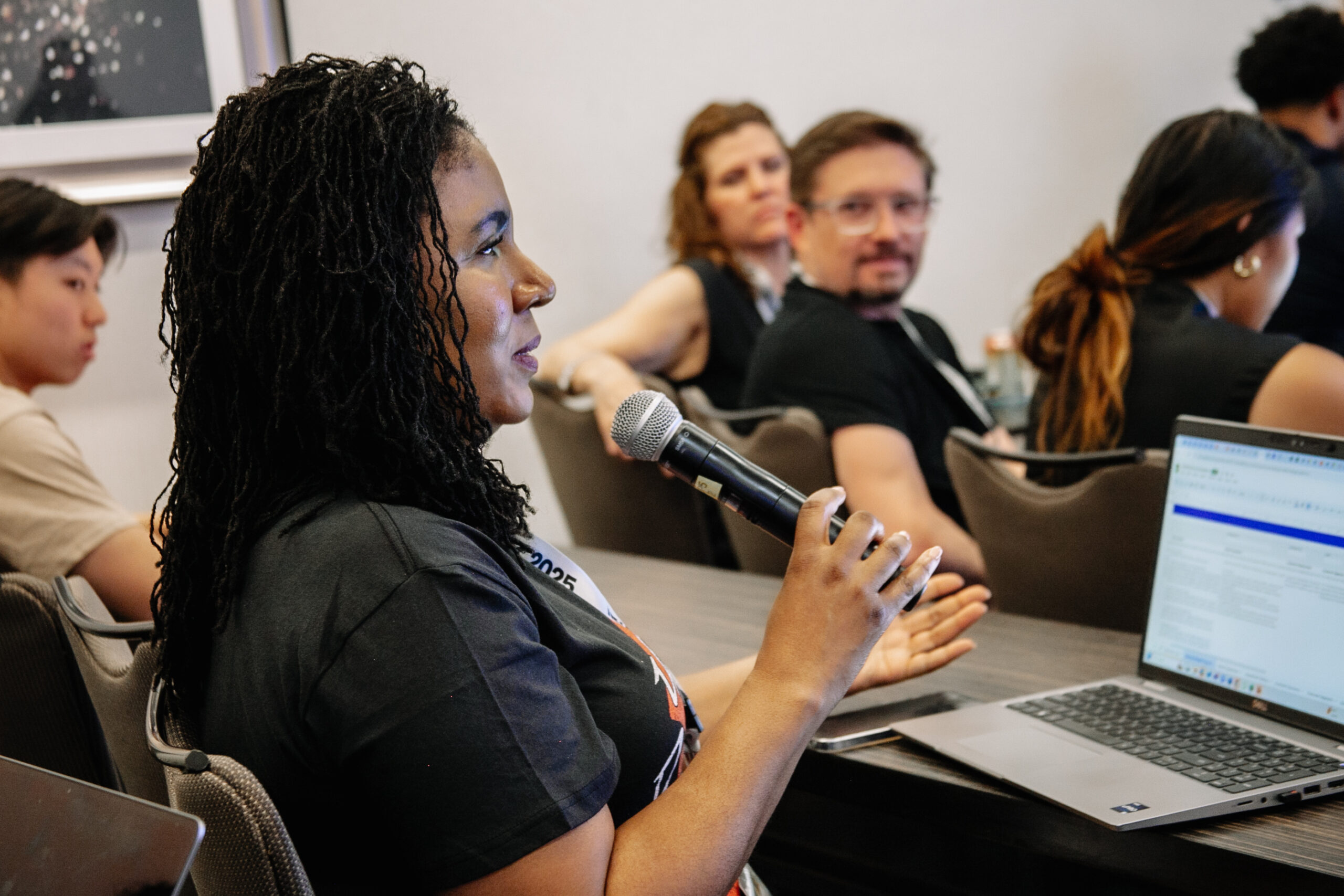 A woman speaking at a conference, standing in front of a laptop.