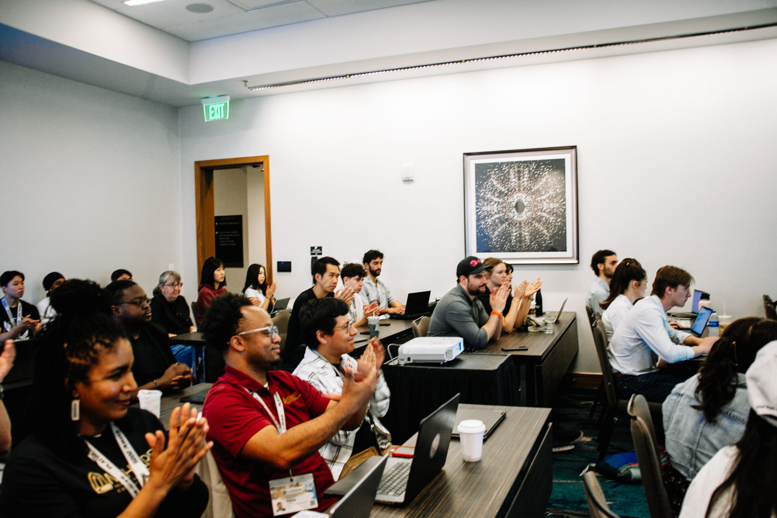 A group of people in a conference room, clapping and seated at tables.