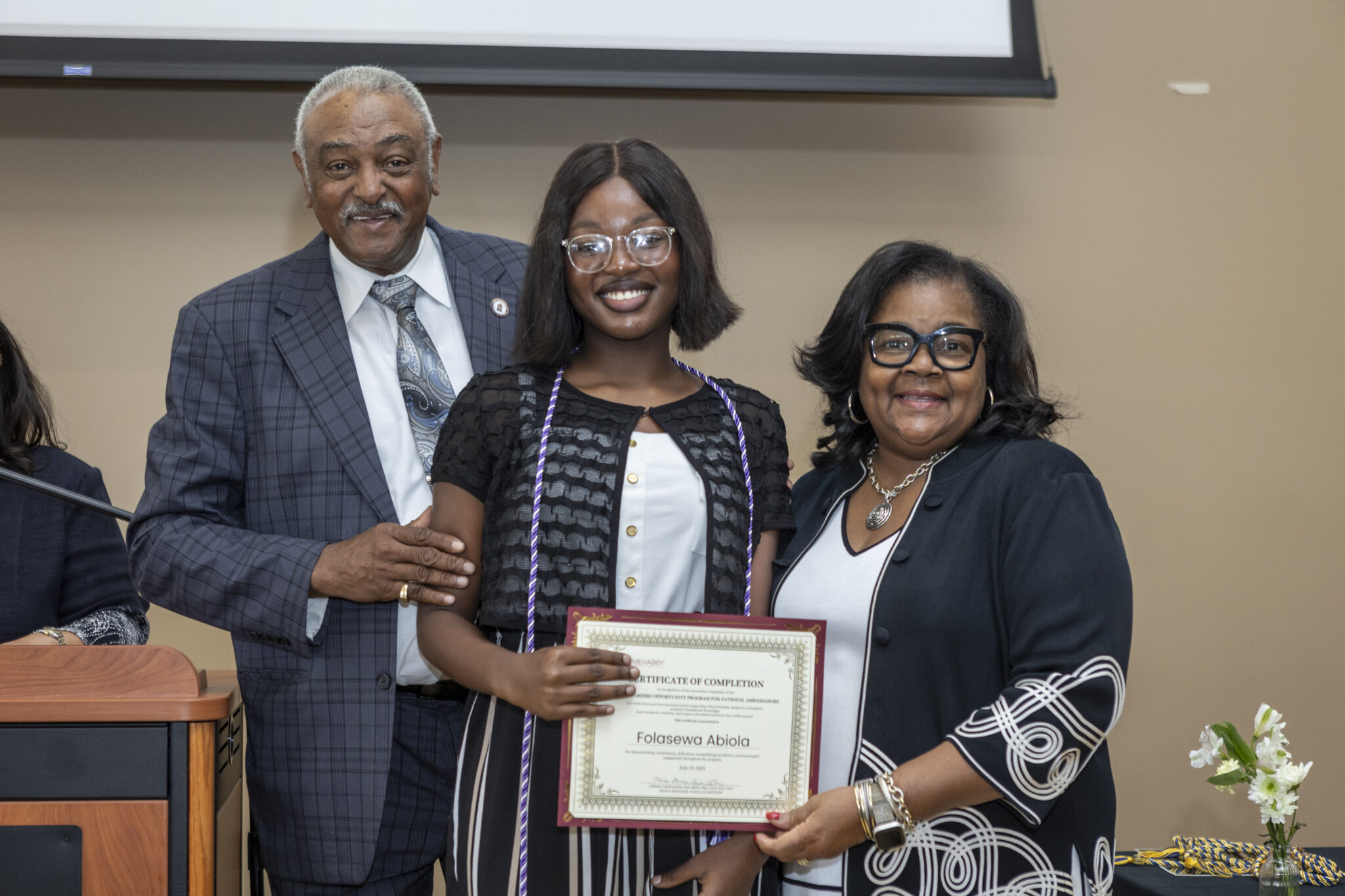 A woman receiving an award from a man and a woman. They are standing in front of a podium.