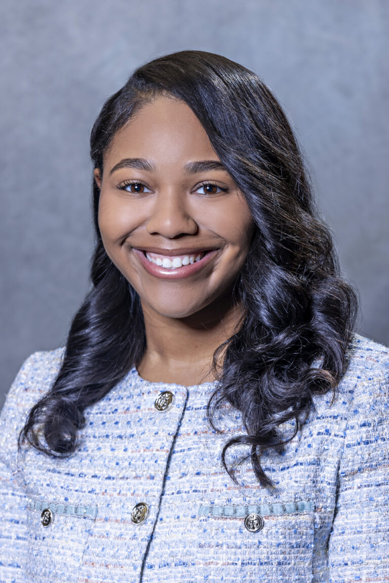A young woman posing for a portrait. She is smiling and wearing a suit.