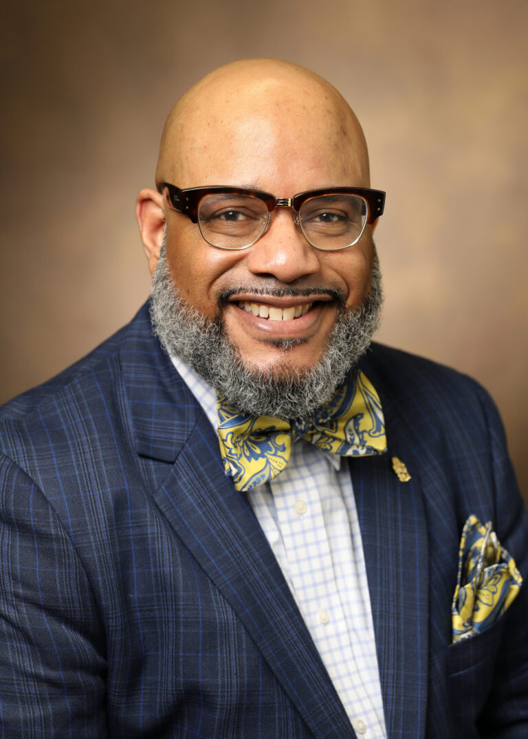Black man in suit and tie, smiling, posing for portrait.