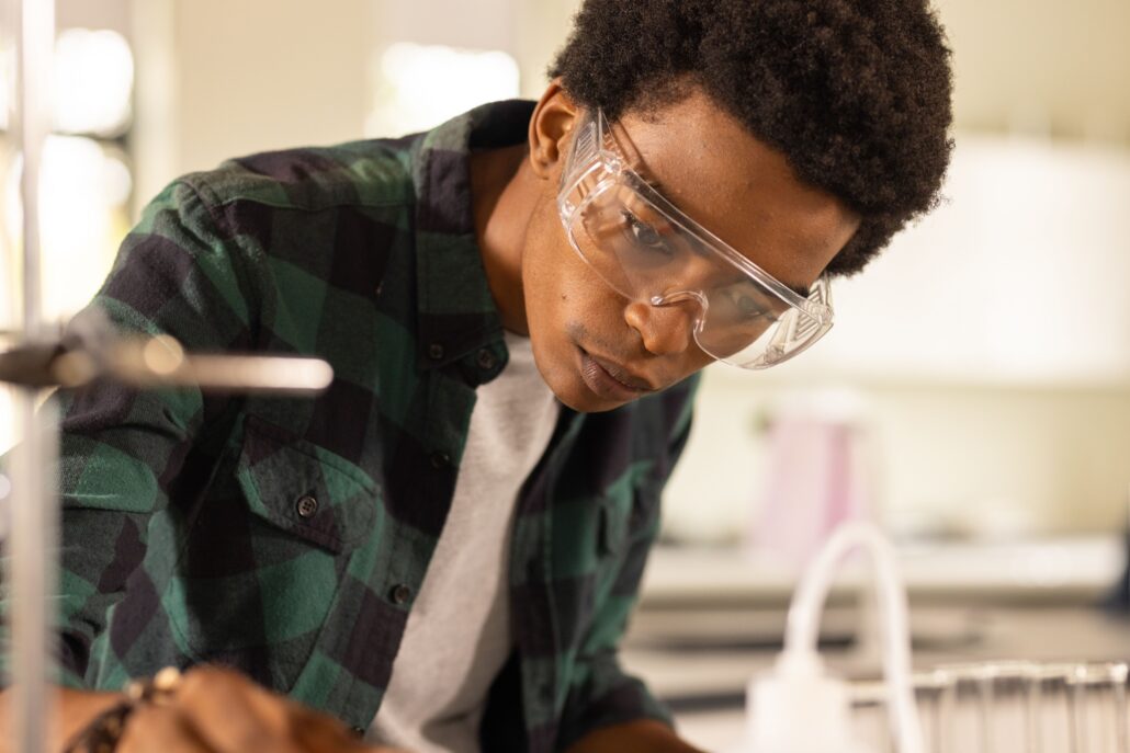 A young man in a lab, wearing glasses and a lab coat, working at a lab bench.