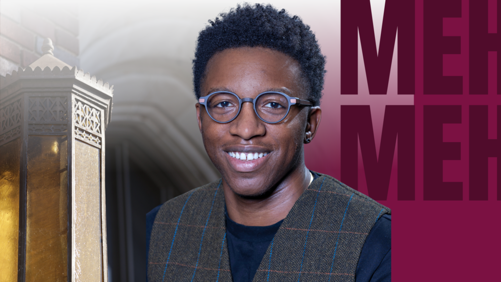 A man in glasses smiling, with a sign behind him that reads "Mehman".